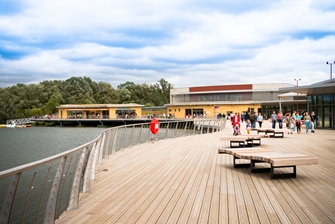 image of a wooden deck next to the water at lakeside, families walking in the background