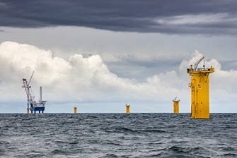 stormy sea, yellow foundations of the wind turbines visible in the foreground, with a crane building a wind turbine in the background
