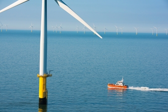 sunny view of the sea, a boat passing a wind turbine closely, with more wind turbines in the background