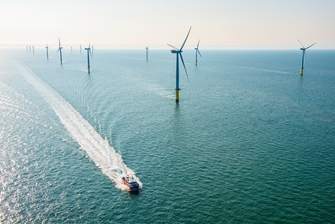 sunny view of the sea, a boat is passing a row of wind turbines, leaving trail waves behind it