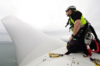 man wearing a harness attached to the wind turbine, inspecting one of the blades