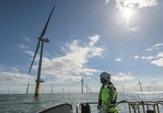 sunny view of the sea, a man on a boat is looking up at one of the many wind turbines visible on the horizon