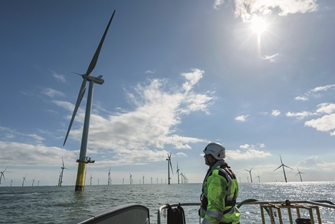 sunny view of the sea, a man on a boat is looking up at one of the many wind turbines visible on the horizon