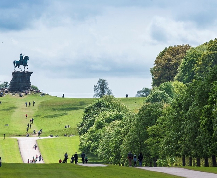 people walking through the park, up a hill to the monument of a rider