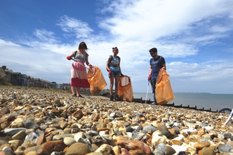 three people picking up rubbish from a pebbled beach