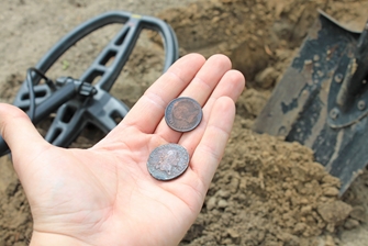 a detectorist holding two found rusted coins in his hand, with a metal detector and a shovel in the background