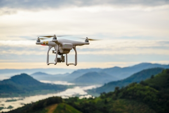 a close up on a drone high up in the sky, with green mountains below it