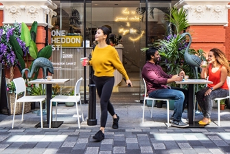 Image of lady with coffee cup and a couple at a table, outside of cafe at One Heddon Street