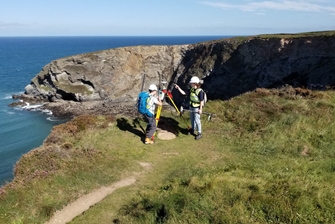 Image of two people standing on the cliffs on the coast, surveying with equipment